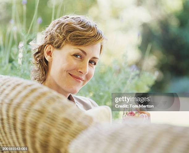 woman relaxing on wicker sofa, holding drink, portrait - wintergarten stock-fotos und bilder