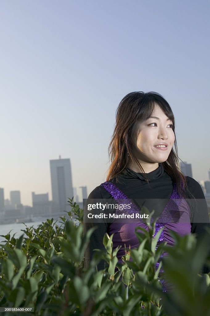 Young woman standing in bushes, city skyline in background