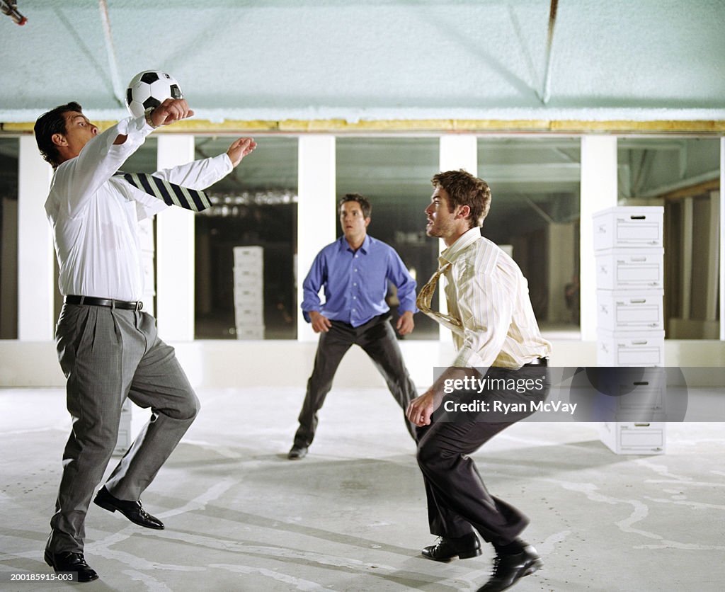 Business colleagues playing soccer in empty office building