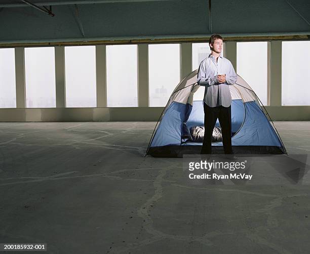 young businessman camping out with tent in empty office space - zeltplatz stock-fotos und bilder