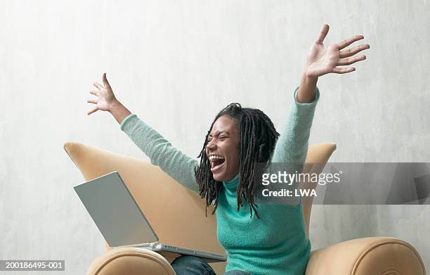 young woman, sitting in armchair with laptop, arms outstretched - entusiasmo fotografías e imágenes de stock
