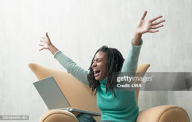 young woman, sitting in armchair with laptop, arms outstretched - excitement photos et images de collection