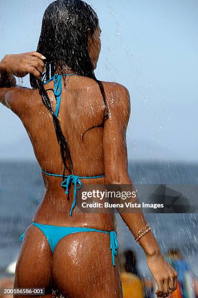 young woman wearing bikini at beach under water spray, rear view - thong stock pictures, royalty-free photos & images