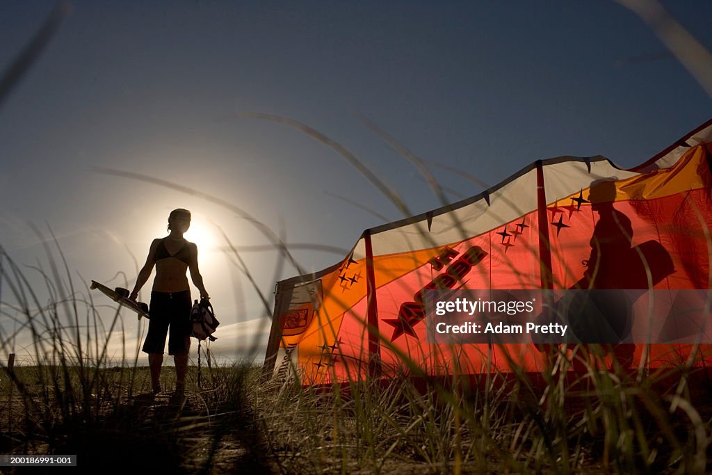 Woman on beach holding kiteboard, man behind wind break