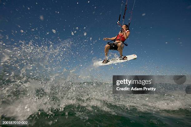 female kiteboarder mid-air, holding line one handed, low angle view - kite surfing stock pictures, royalty-free photos & images