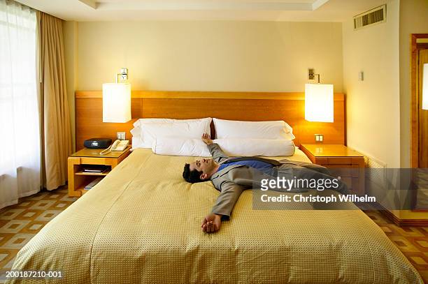 businessman sleeping on hotel bed, arms outstretched, side view - bed side view stock pictures, royalty-free photos & images