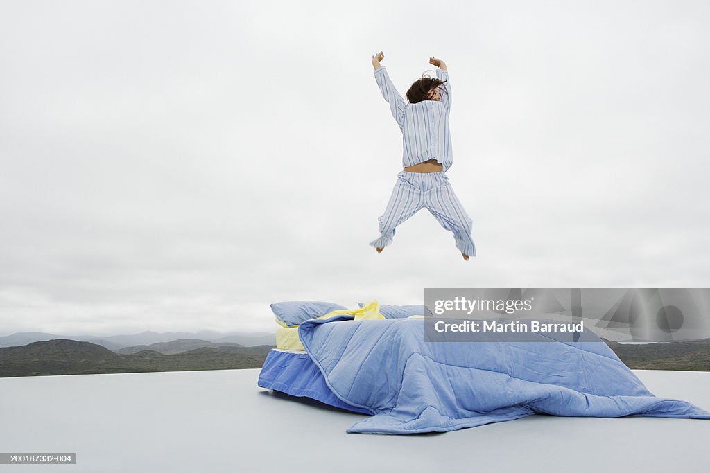 Woman jumping on double bed on platform in rugged landscape