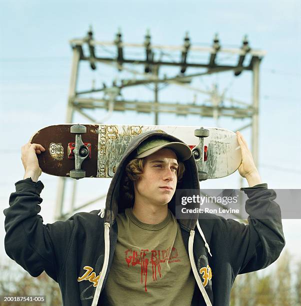 teenage boy (16-18) holding skateboard behind head - hoodie boy stock pictures, royalty-free photos & images