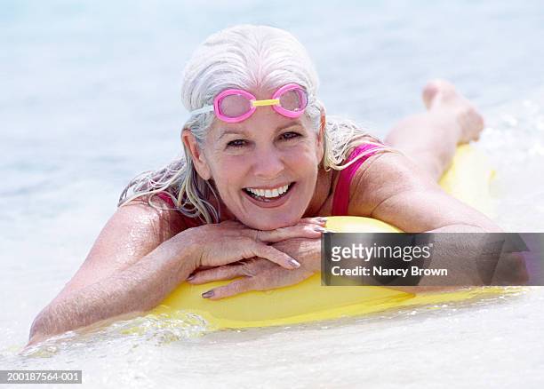 senior woman floating on raft in sea, portrait - alte frau badeanzug stock-fotos und bilder