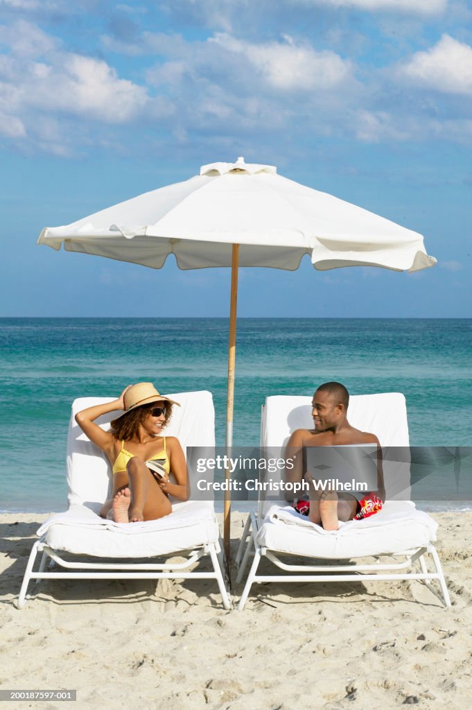 Couple sitting under umbrella on beach with laptop
