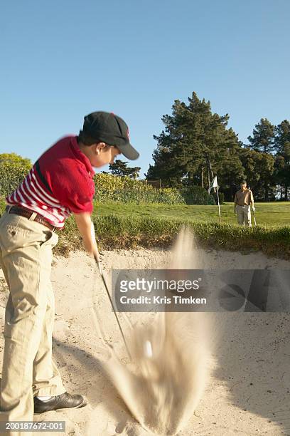 boy (11-13) hitting golf ball out of sand trap, father in background - バンカーショット ストックフォトと画像