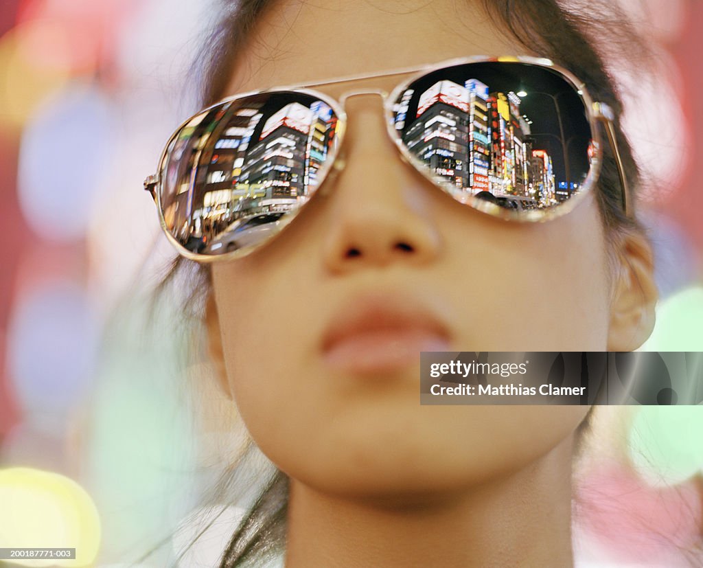 Young woman wearing sunglasses, close-up signage reflected in glasses