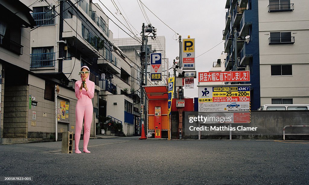 Young woman on street wearing pink alien costume, pointing gun