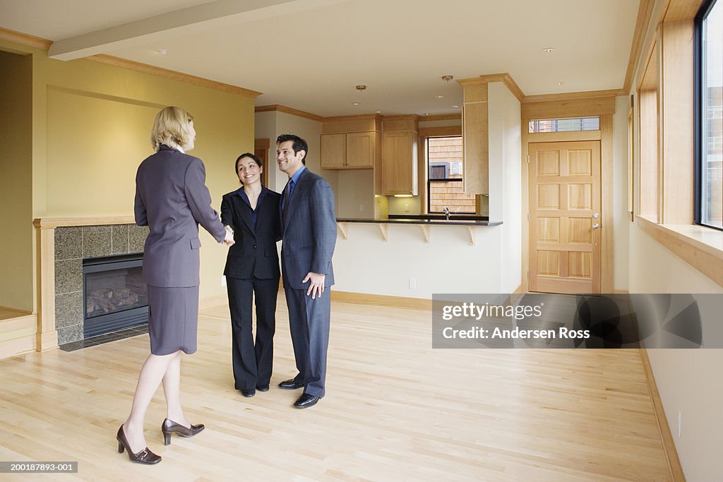 Man and woman in empty house, shaking hands with female Real Estate Agent