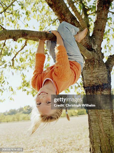 girl (8-10) hanging upside down from tree, smiling, portrait - girls barefoot in jeans stockfoto's en -beelden