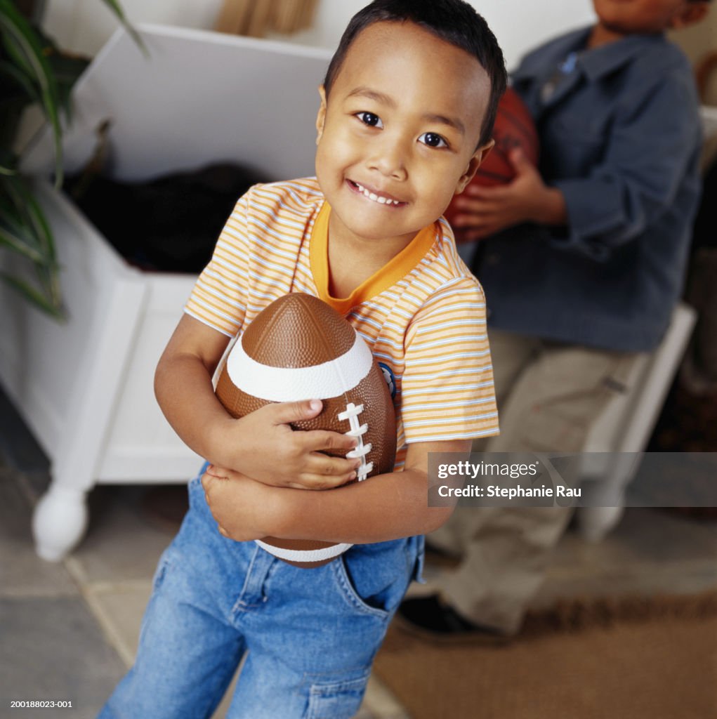 Boy (5-7) holding football, portrait