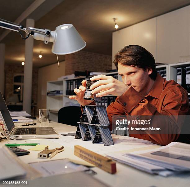 young man at office desk, building house of cards - posizionare foto e immagini stock