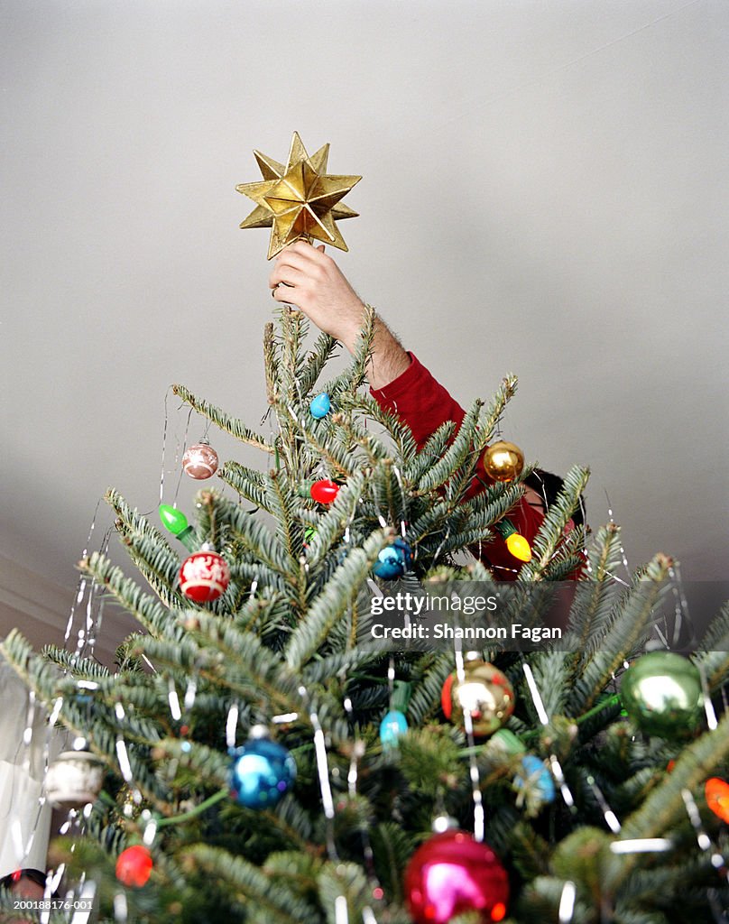 Teenage boy (14-16) putting star on Christmas tree