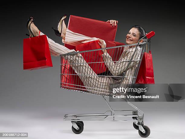 young woman in shopping trolley full of packages, smiling, portrait - shopaholic woman stock pictures, royalty-free photos & images