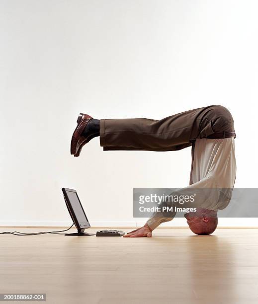 senior man standing on head, looking at laptop, side view - crazy man computer stock pictures, royalty-free photos & images