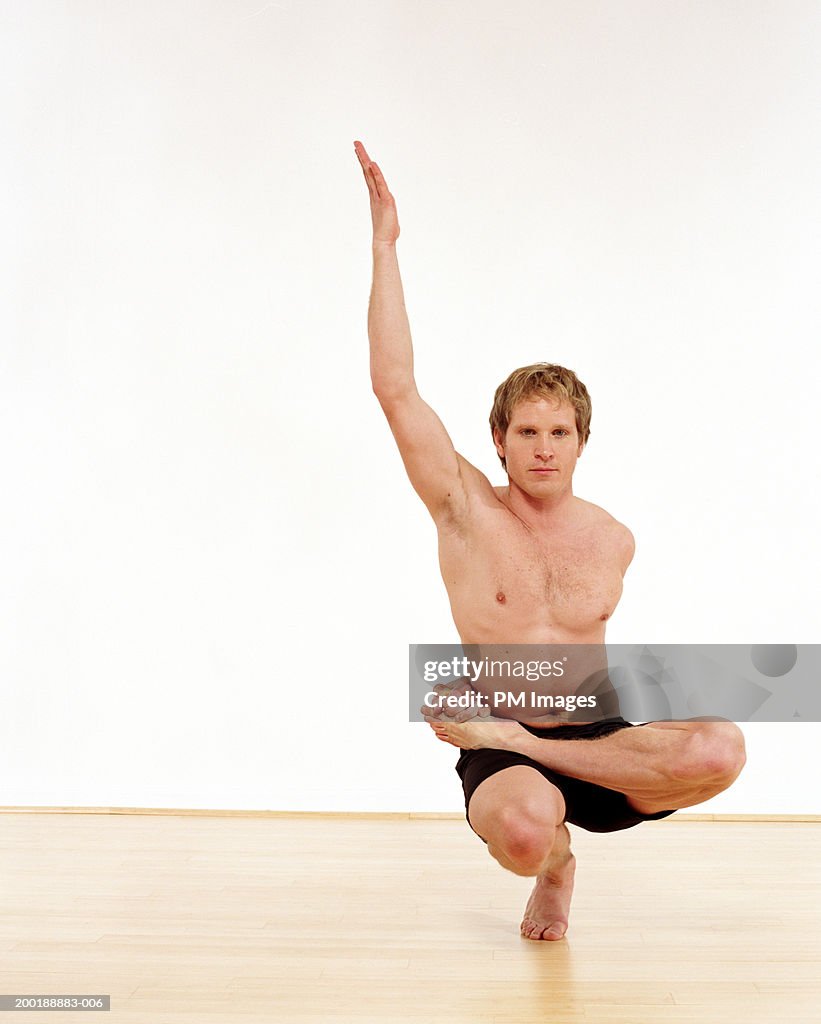 Man performing one legged squat with arm raised upward, portrait