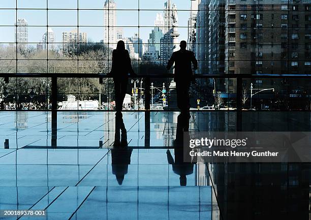 silhouette of two people in lobby looking through window, rear view - henry mull stock pictures, royalty-free photos & images