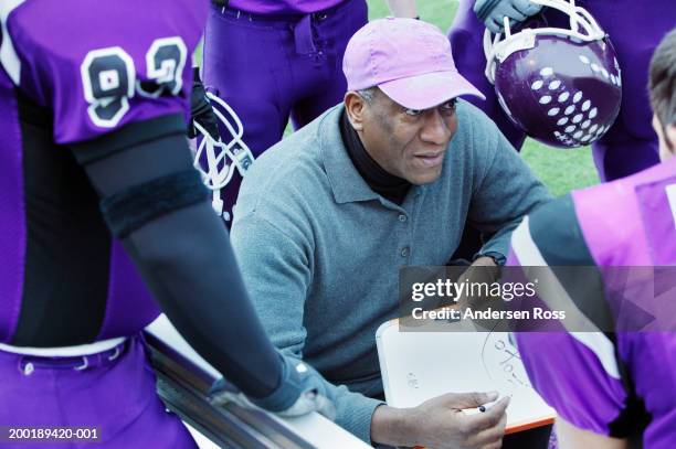 foorball coach crouching in huddle, talking to team - team sport huddle stock pictures, royalty-free photos & images