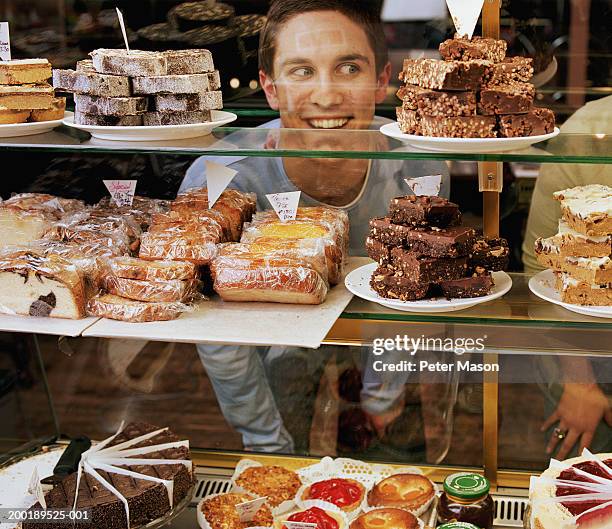 young man with nose pressed against glass looking at cakes, smiling - bakery window stock pictures, royalty-free photos & images