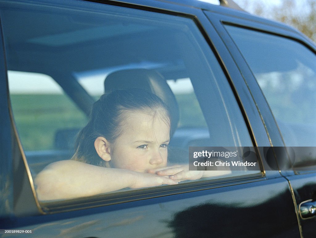 Girl (7-9) sitting in car, looking out window, view through window