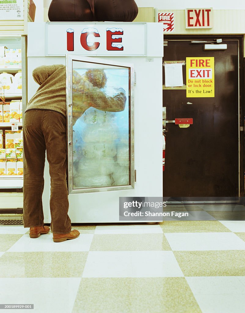Young man searching in supermarket freezer for ice, rear view