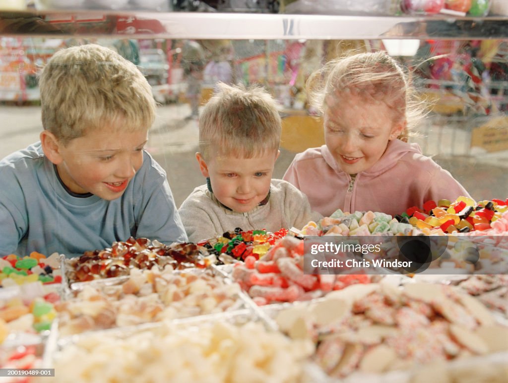 Two boys (4-8) and girl (7-9) looking at sweets in glass counter