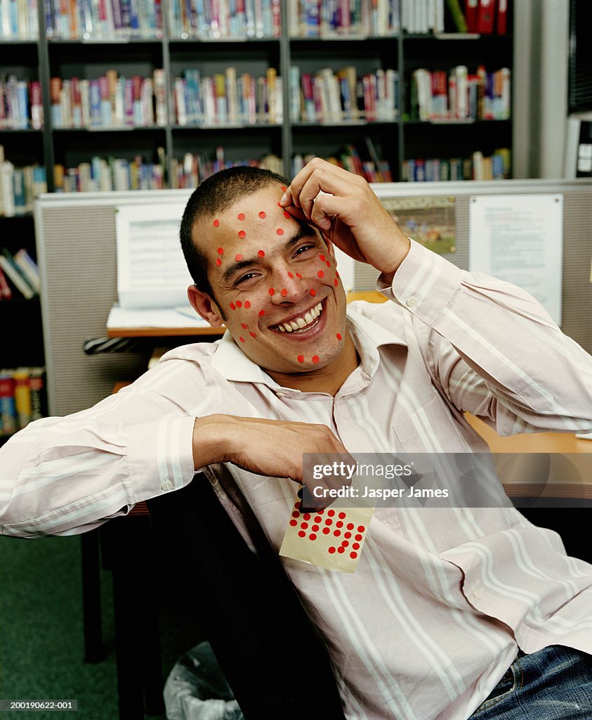 Man in office, putting red sticker spots on face, smiling, portrait