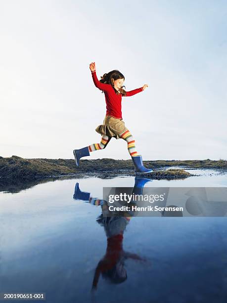 girl (8-10) arms raised, leaping over water onto grassy mound - kids in undies stockfoto's en -beelden