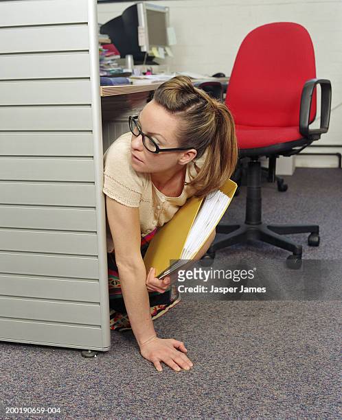 businesswoman under desk in office, holding yellow folder - paranoia stock-fotos und bilder