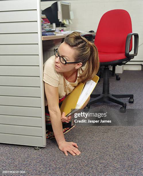 businesswoman under desk in office, holding yellow folder - paranoia stock pictures, royalty-free photos & images