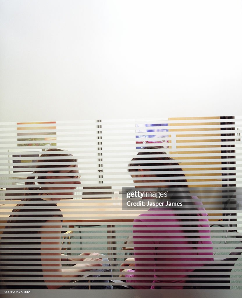 Two businesswomen in meeting room, view through glass