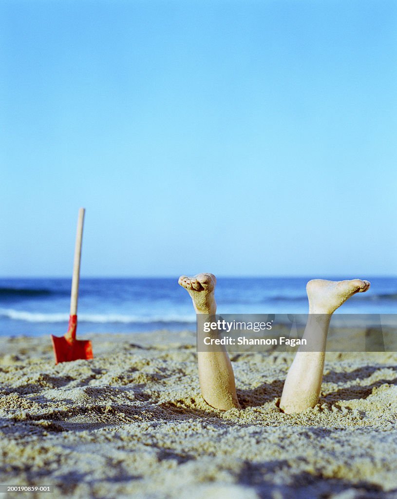 Young woman buried upside down in sand, feet sticking out