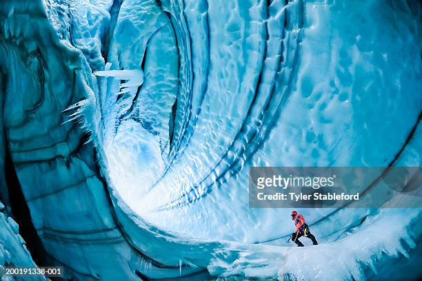 male ice climber exploring ice cave, low angle view - esplorazione foto e immagini stock
