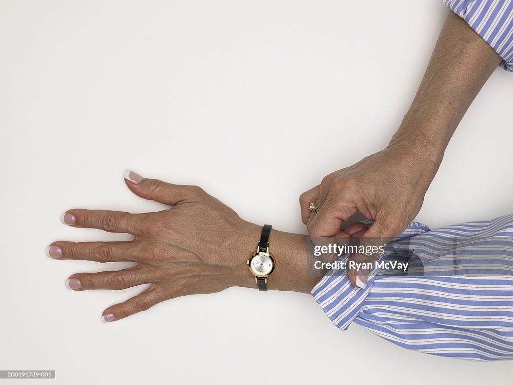 Mature woman folding cuff of shirt, close-up of hands