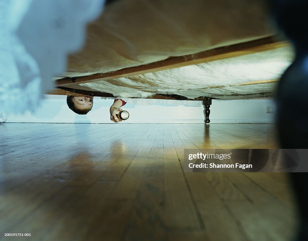 Boy (10-12) looking under bed with flashlight, ground view