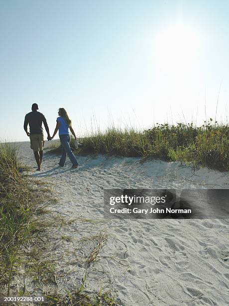 young couple holding hands walking along path to beach, rear view - couple dunes stock-fotos und bilder