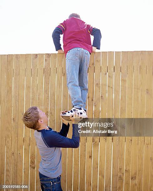 boy (11-13) helping another boy (10-12) climb fence, rear view - 12 stock-fotos und bilder