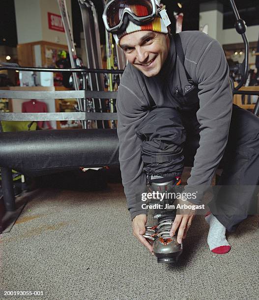man putting on ski boots in shop, smiling, portrait - skischoen stockfoto's en -beelden