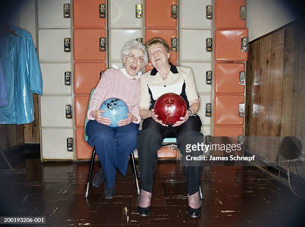 Two elderly women with bowling balls in locker room, smiling, portrait