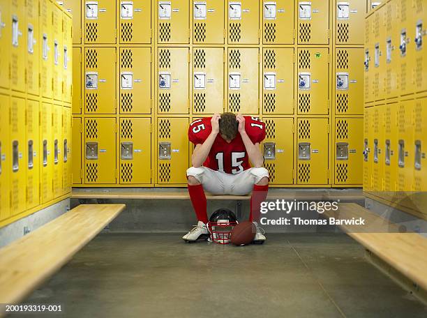teenage football player (15-17) hanging head in locker room - banco de jogadores fotografías e imágenes de stock