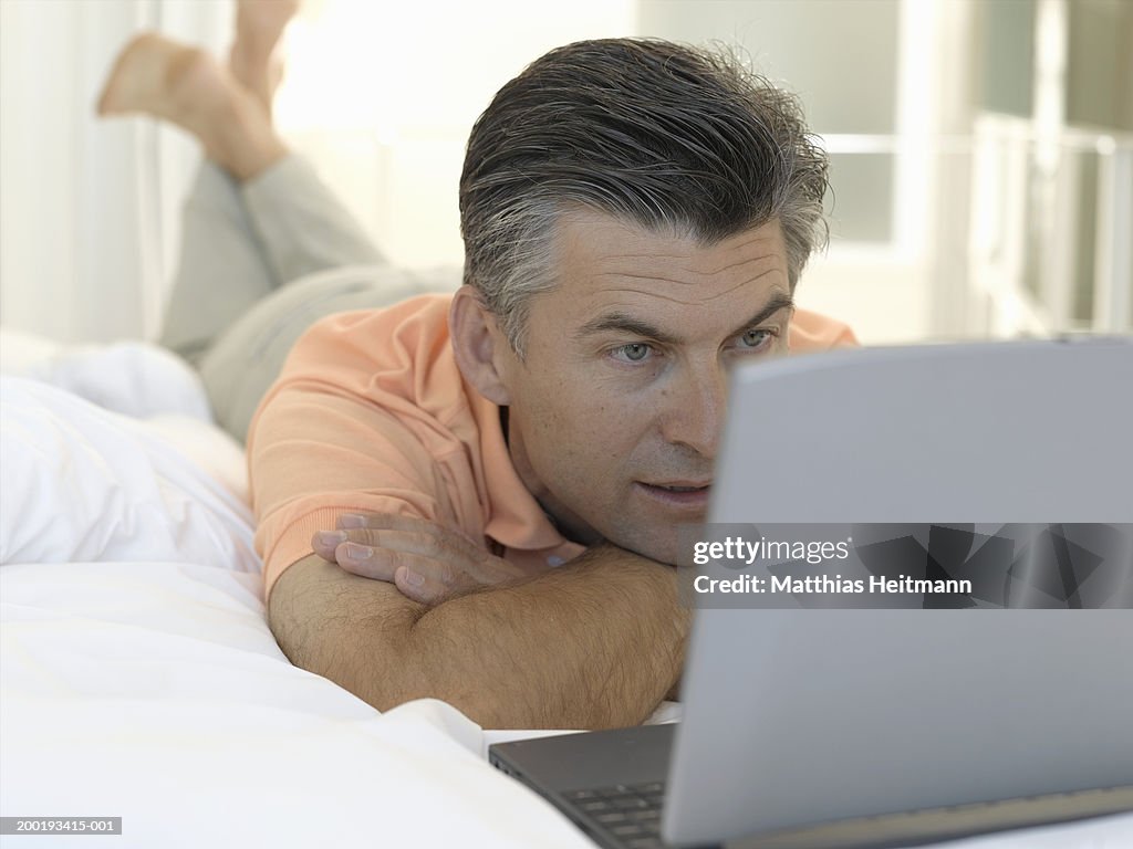 Mature man lying on bed looking at laptop computer, close-up
