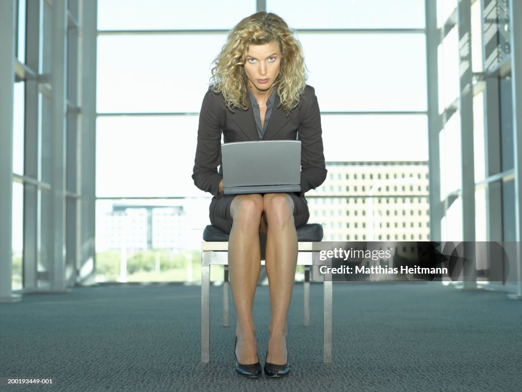 Young businesswoman sitting on bench using laptop, indoors, portrait