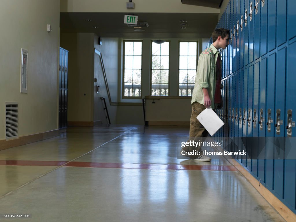 Teenage boy (12-14) leaning head against lockers in hallway, side view