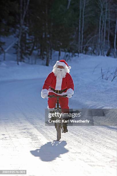 mature man in santa costume riding bicycle on snow-covered roadway - santa riding stock pictures, royalty-free photos & images