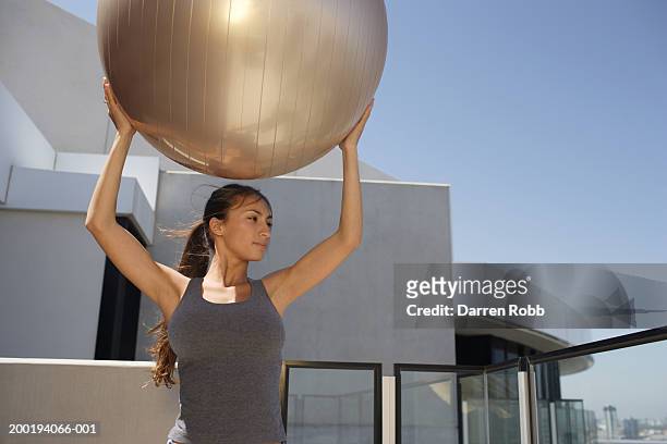 young woman holding exercise ball over head on balcony - yoga ball outside stock pictures, royalty-free photos & images